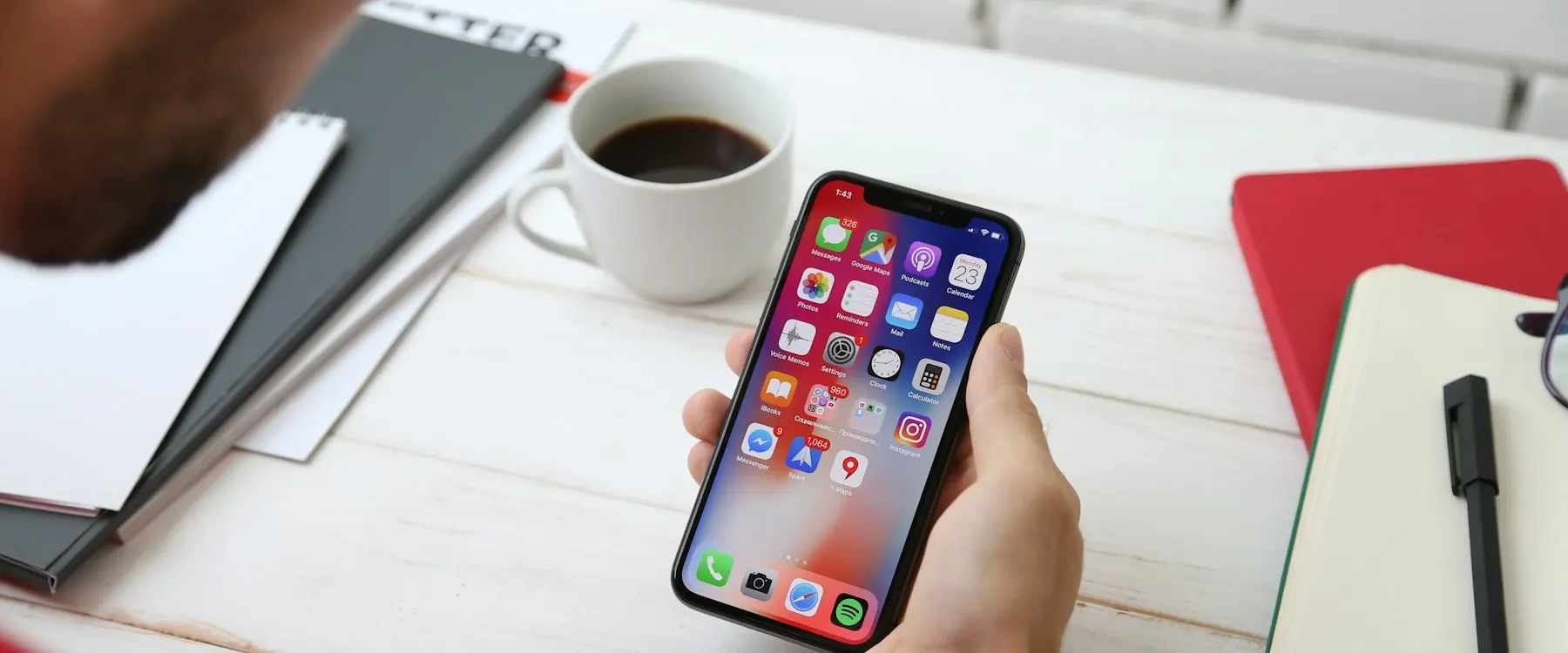 Une main tenant un smartphone au-dessus d’un bureau